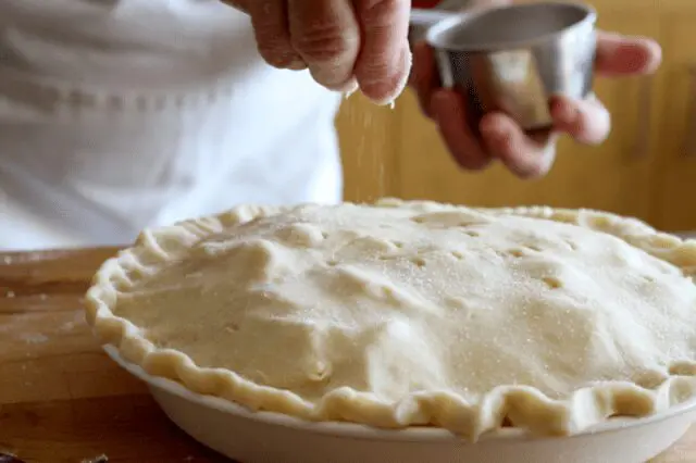 Betty Kandt sprinkles sugar on an apple pie for Pi Day
