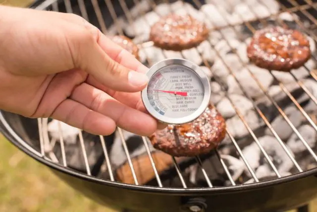 meat thermometer in burger on grill. shows importance of food safety.