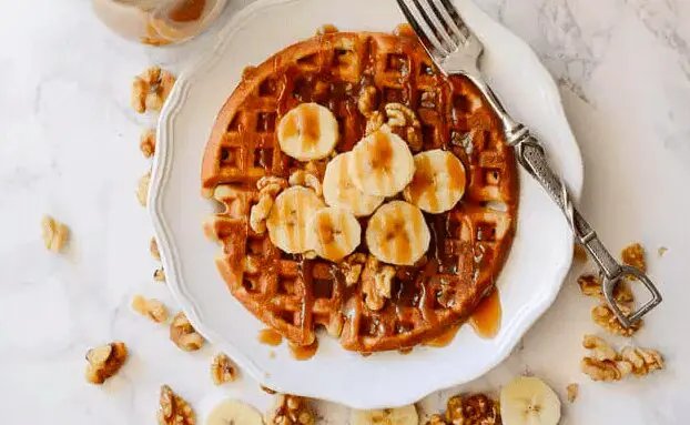 Banana Bread Waffles with Brown Sugar Caramel Syrup on a white plate with a fork. This is one of our unique waffle recipes