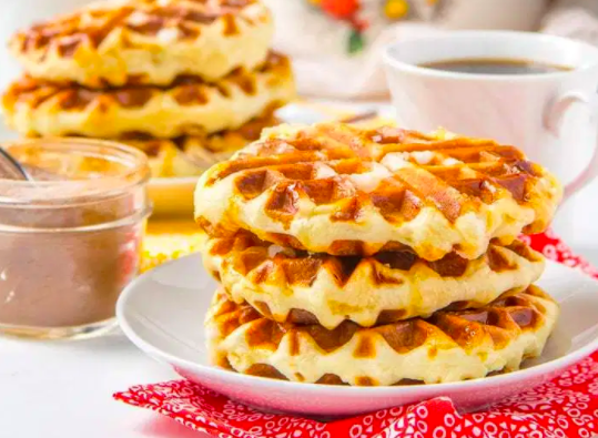 Three belgian waffles on white plate with waffles, coffee and drizzle in the background. Unique Waffle Recipe