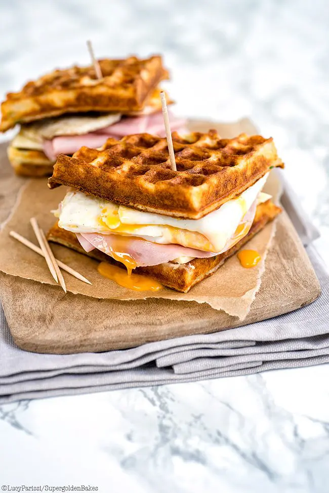 PARMESAN WAFFLE, HAM, CHEESE AND EGG BREAKFAST SANDWICH on a cutting board