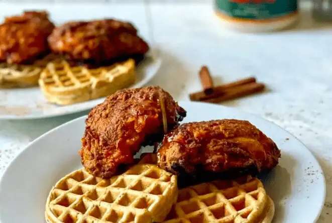 Nashville style hot chicken and waffles being drizzles with maple syrup on a white plate