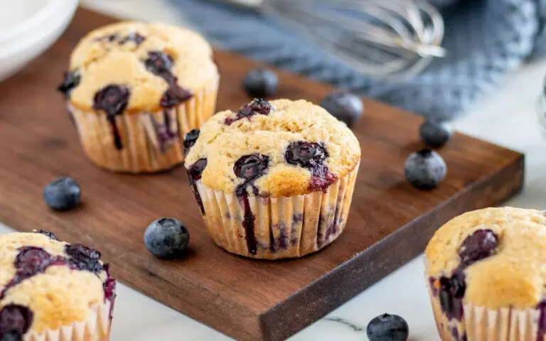 Whole Wheat Blueberry muffins on a serving tray with Blueberries sprinkled around.