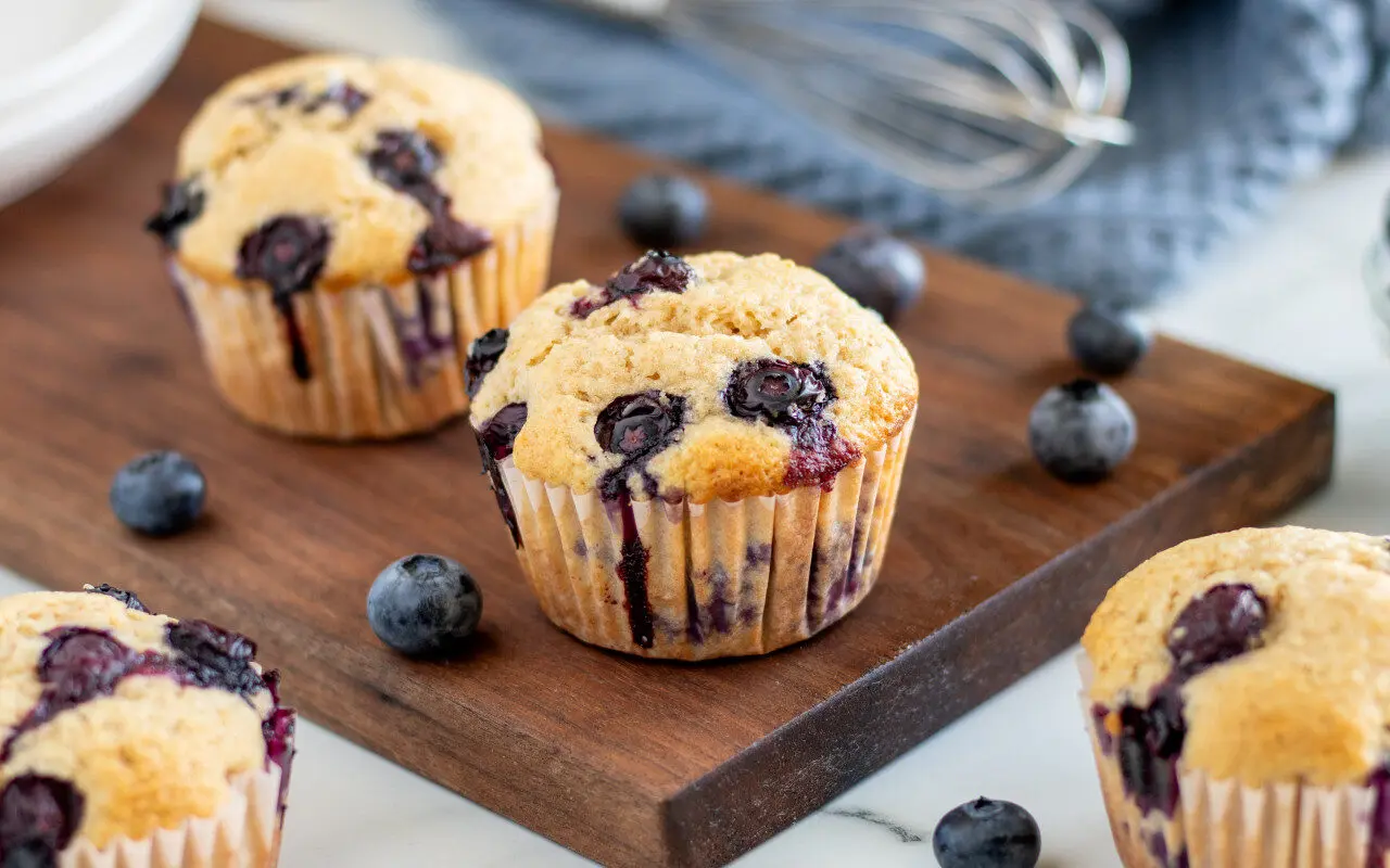 Whole Wheat Blueberry muffins on a serving tray with Blueberries sprinkled around.