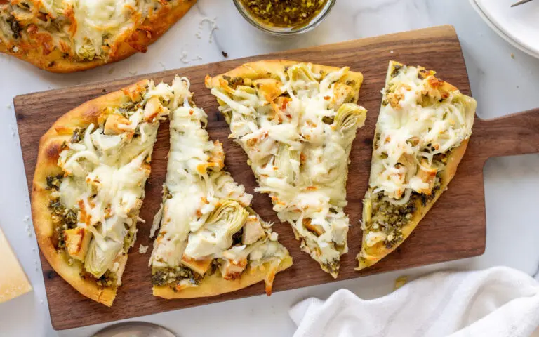 Chicken Artichoke Naan Pizza split into 4 pieces on a serving tray against a marble background.