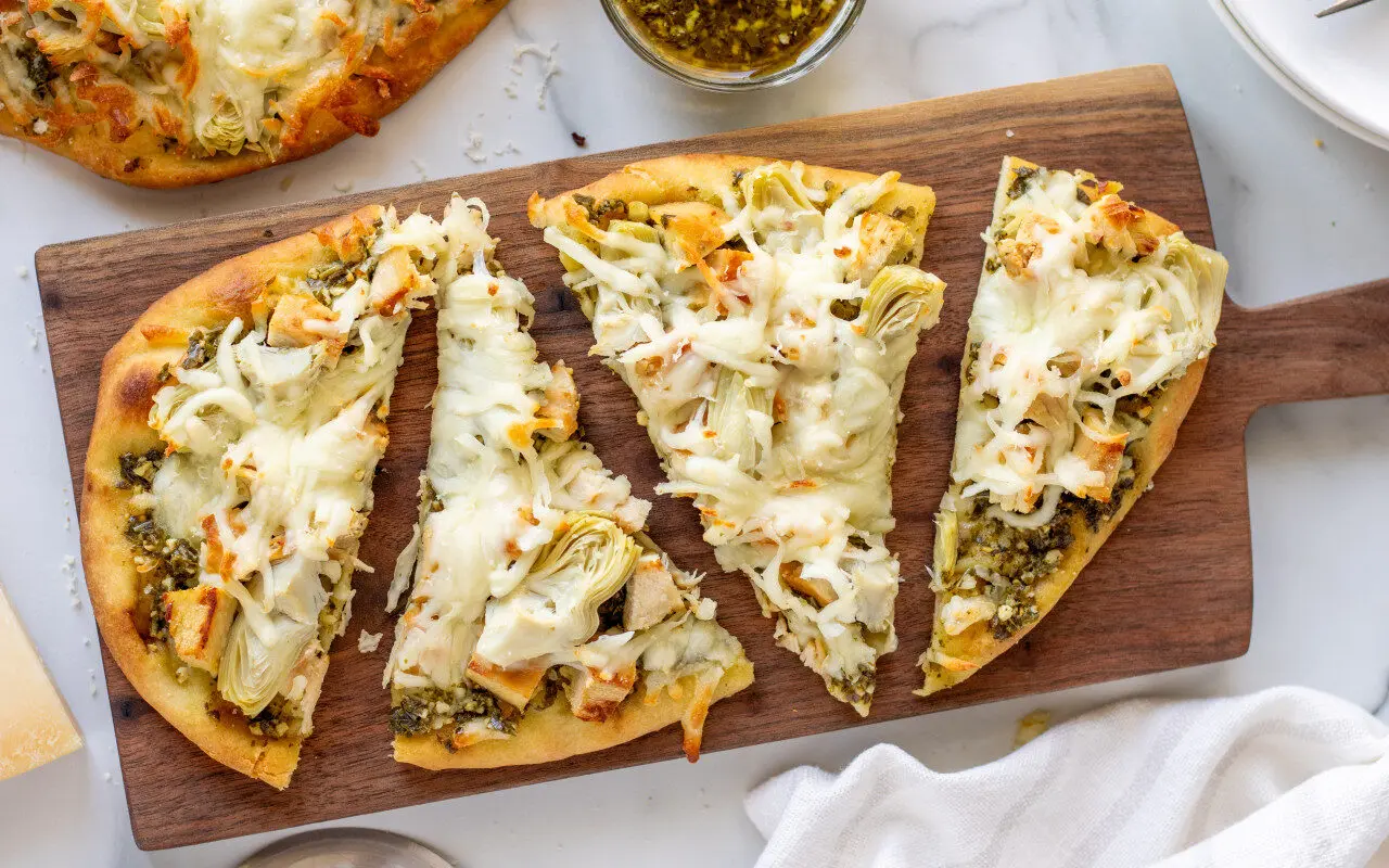 Chicken Artichoke Naan Pizza split into 4 pieces on a serving tray against a marble background.