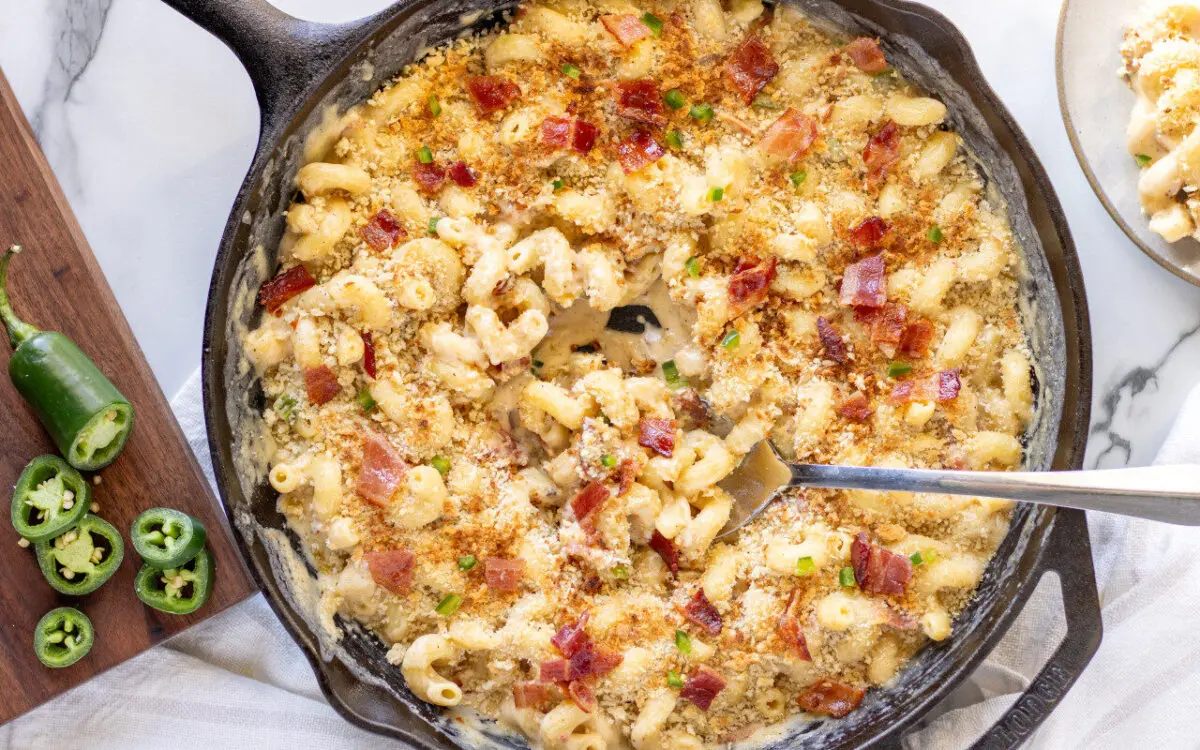 Spicy Mac in Cheese baked in a cast iron skillet with a serving spoon inserted inside.
