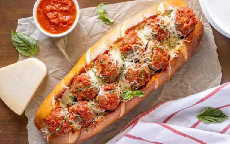 Giant Meatball Sandwich on a serving tray with cheese and mozzarella sauce in a bowl around it.