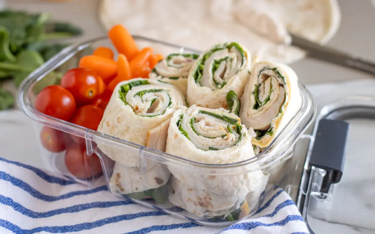Lunchbox Turkey Pinwheels in a container with tomatoes and carrots.
