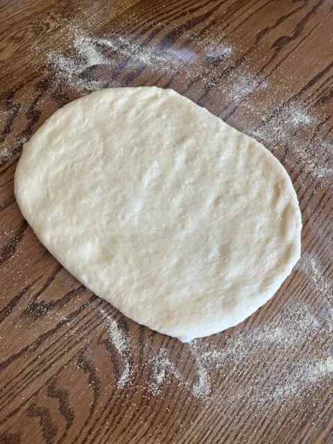 Homemade English Muffin dough laid out on top of corn meal ready to be patted and cut into rounds. 