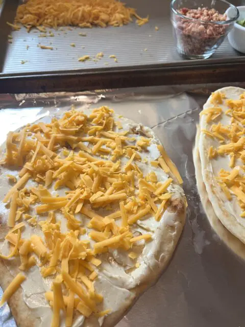 Loaded Potato Naan Pizzas on a tray with the garlic and herb cheese was spread and cheese sprinkled on.