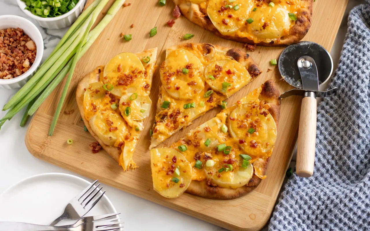 Loased Potato Naan Pizza on a cutting board cut into three slices with chives and bacon for topping.