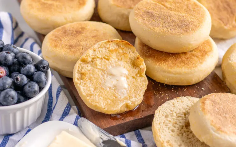 English muffins with a slab of melted butter sitting on a wooden serving board with blueberries on the side.