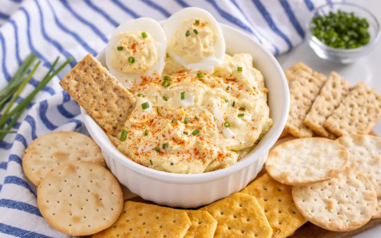 Deviled Egg Dip | Eat Wheat Simple Devlied Egg Dip in a bowl with crackers spread around. Blue and white striped towel is featured in the background.