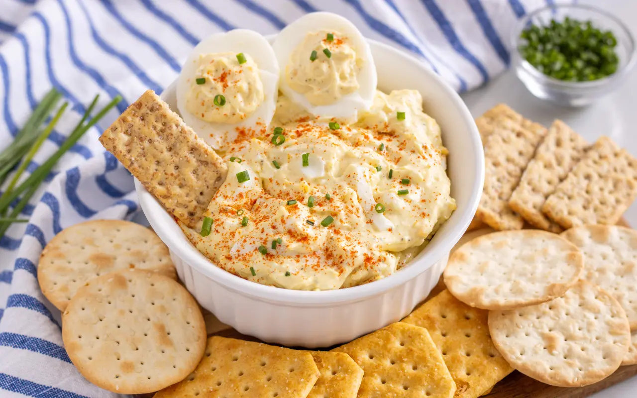 Deviled Egg Dip | Eat Wheat Simple Devlied Egg Dip in a bowl with crackers spread around. Blue and white striped towel is featured in the background.