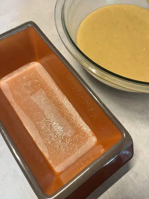 Wet and dry ingredients for the Honey Spice Bread in the mixing bowl next to the prepared 8x4 baking pan.