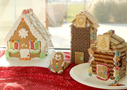 A Gingerbread house made with a kit, a clock tower made with graham crackers and a log cabin made with pretzel sticks