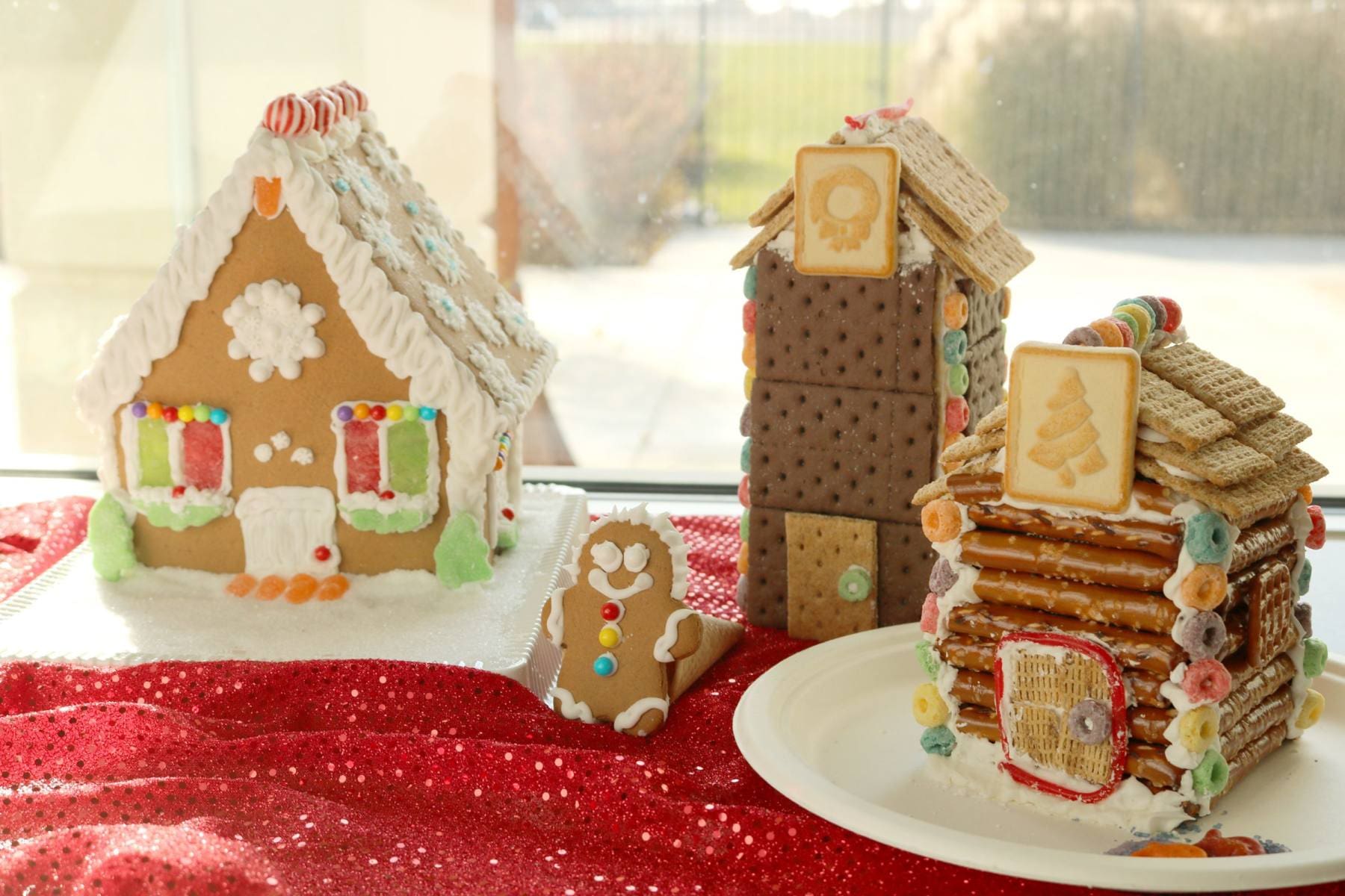 A Gingerbread house made with a kit, a clock tower made with graham crackers and a log cabin made with pretzel sticks