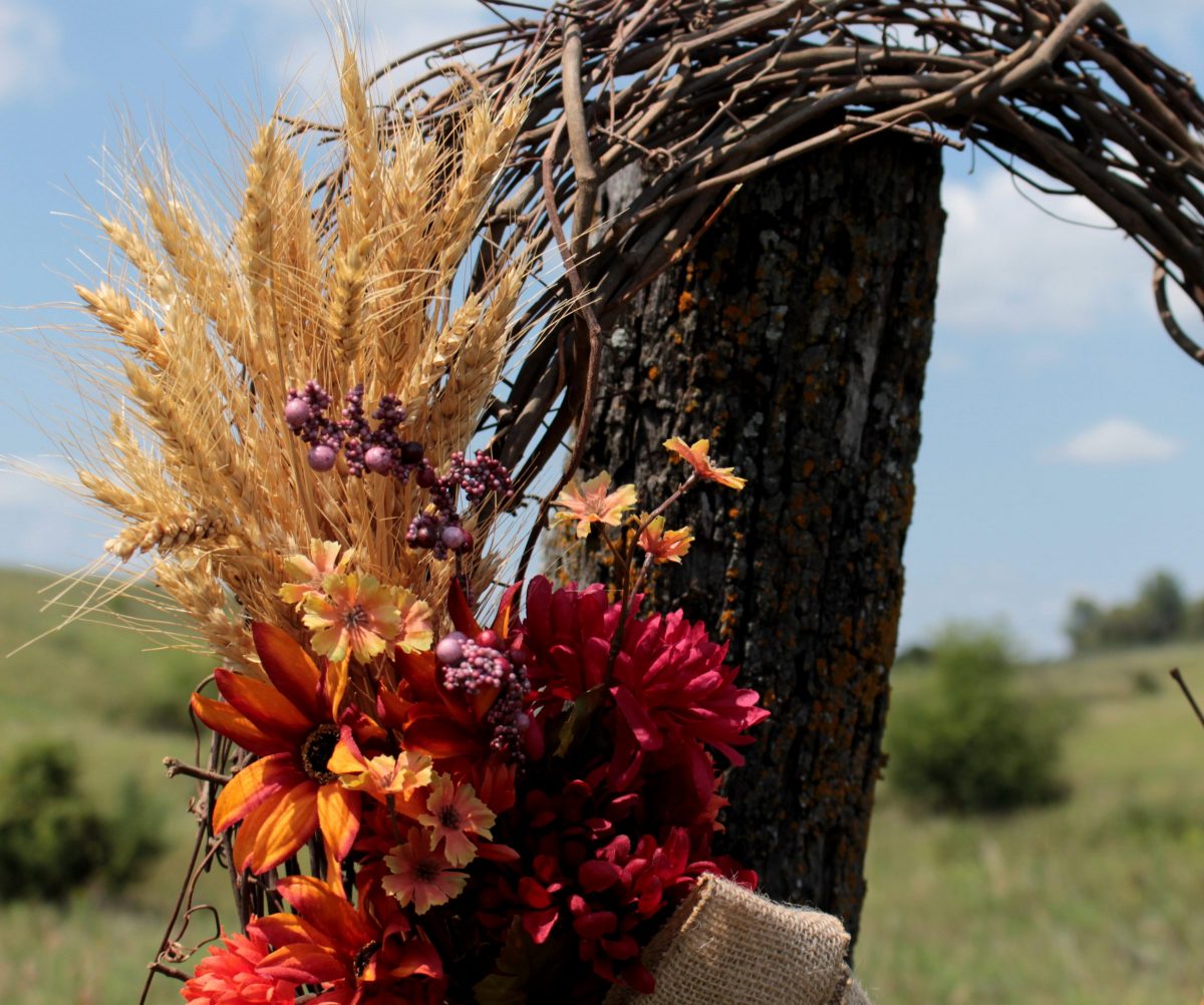 A rustic wheat wreat hung on a fence post in front of a Kansas pasture