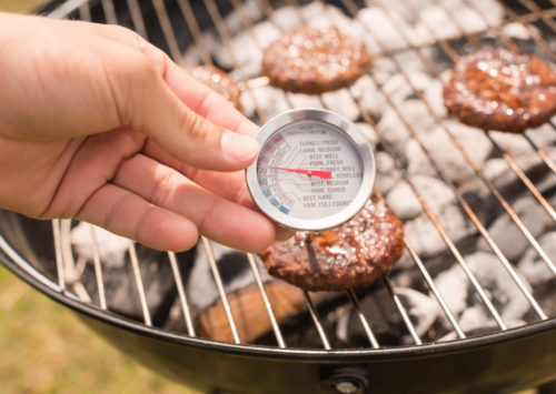 meat thermometer in burger on grill. shows importance of food safety.