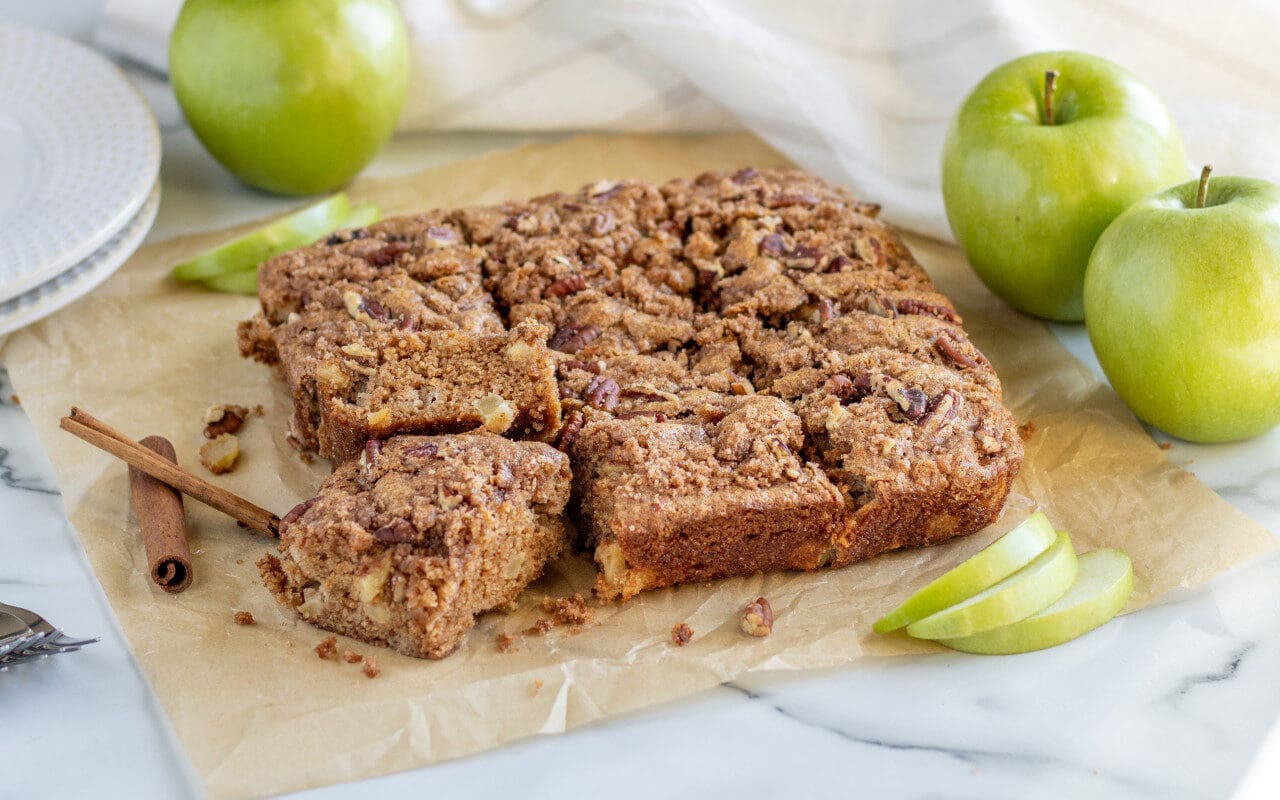 Whole Wheat Apple Cinnamon Cake sliced into bars with apples in the background.