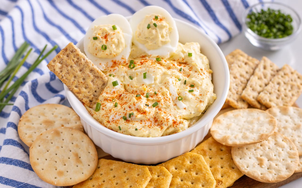 Simple Devlied Egg Dip in a bowl with crackers spread around. Blue and white striped towel is featured in the background.