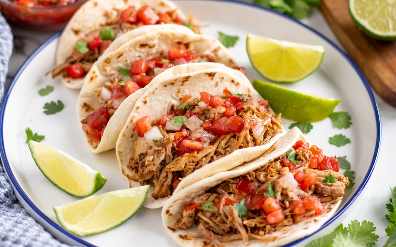 Pork Carnitas Street Tacos served on a plate with pico de gallo on top and limes to the side.